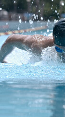 Mid-shot swimmer slices through water, creating splashes, focused during outdoor pool training.