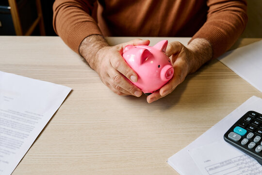 Man holding piggy bank at table with bills and calculator at home