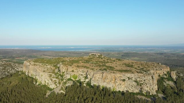 Wide aerial shot of the rocky cliffs and plateau at Chateau de Opoul Perillos, with expansive landscape and distant coastline under a clear blue sky.