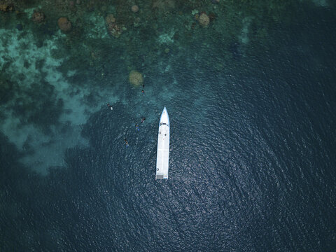 Aerial view of a white yacht slicing through the dark blue sea, contrasting with the lighter turquoise waters near the coral reefs, Karimunjawa, Central Java, Indonesia.