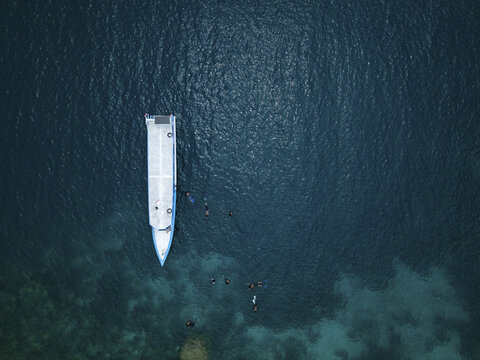Aerial view of a boat surrounded by dark blue waters and snorkelers, creating a striking contrast against the vibrant seabed, Karimunjawa, Central Java, Indonesia.