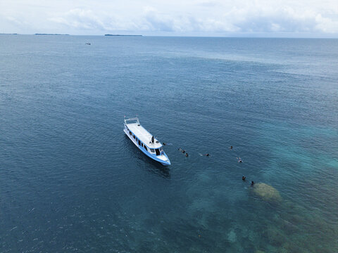Aerial view of a brilliant white and blue boat floating on the turquoise sea near Cemara Kecil Snorkeling Spot, Karimunjawa, Central Java, Indonesia.