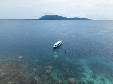 Aerial view of a pristine turquoise sea with a boat anchored near the vibrant coral reefs, Cemara Kecil Snorkeling Spot, Karimunjawa, Central Java, Indonesia.