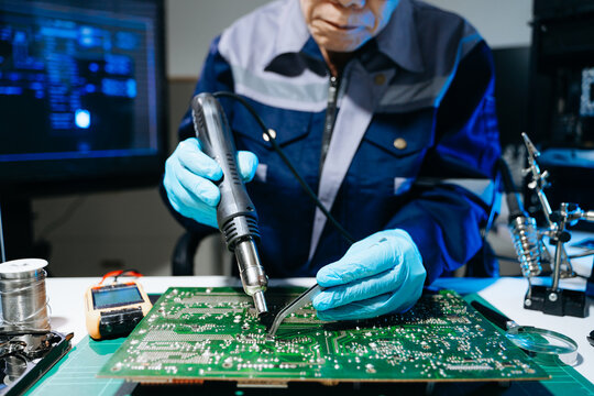 Senior technician performing PCB soldering and diagnostics with multimeter in electronics lab, showcasing hardware engineering