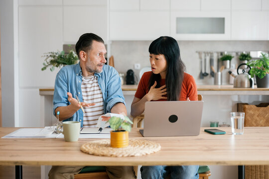 Couple discussing financial problems and bills using laptop in kitchen
