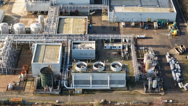 Aerial view of industrial architecture featuring tanks, cooling towers, and interconnected walkways casting shadows under a clear sky, Grimsby, England, United Kingdom.
