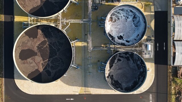 Aerial view of circular tanks filled with swirling, dark water contrasting against the beige surroundings, Lenzing Fibers, Grimsby, England, United Kingdom.