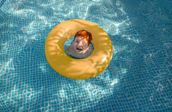 Red-haired child smiling in yellow swimming ring in outdoor pool