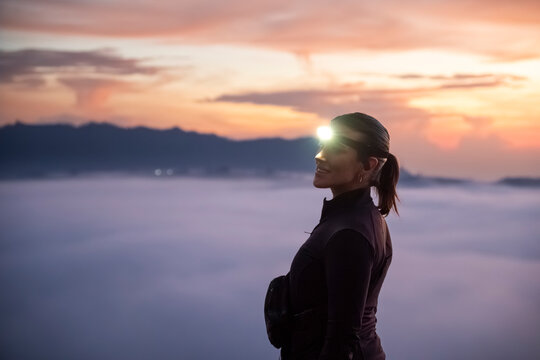 Person with headlamp standing on misty mountain summit at sunrise