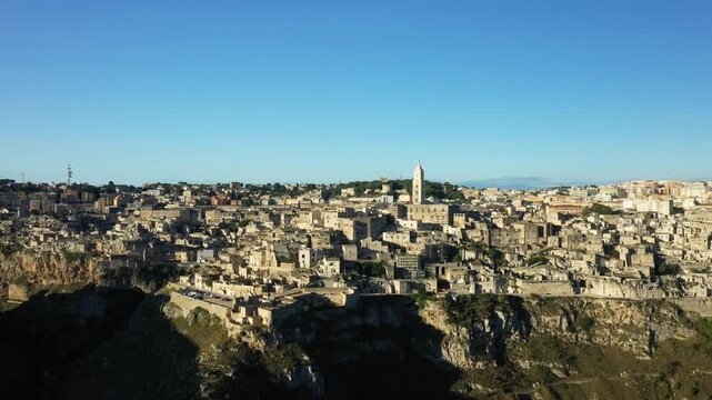 Wide aerial panorama of Matera, Italy, showcasing ancient stone buildings and dramatic cliffs under a clear blue sky.