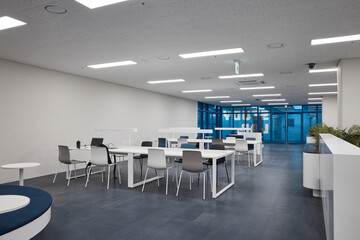 Modern office cafeteria or break room with tables, chairs and daylight.