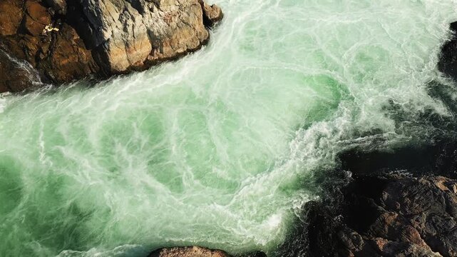 Powerful turquoise rapids rush between dark rocks at Tat Somphamit Waterfalls, Laos, illuminated by early morning sunlight.
