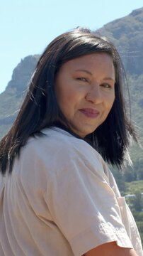 Vertical video: Turning woman after camera cue, posing and smiling at ridge, tan shirt green top