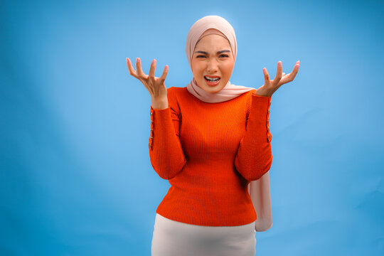 Upset young Asian Muslim woman in a hijab and orange sweater is expressing her anger.