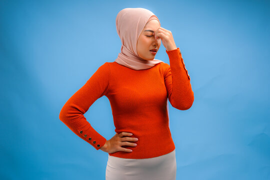 Stressful young Asian Muslim woman in a hijab is looking confused and having headache.