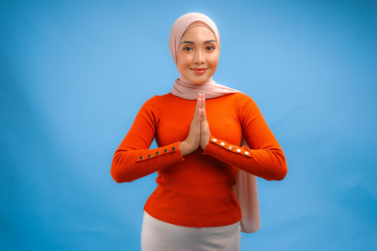 Beautiful Asian Muslim woman smiling to the camera and gesturing traditional greeting.