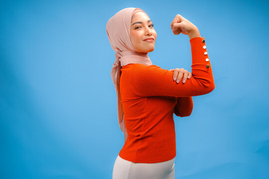 Confident Asian Muslim woman showing strong gesture by lifting her arms and muscles.