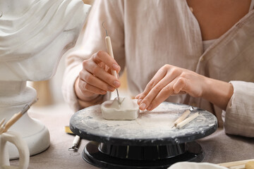 Female sculptor making figure at table in workshop, closeup