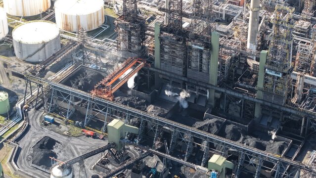 Aerial view of industrial architecture casting long shadows over the dark coal piles and steam rising, Humber Refinery, Immingham, United Kingdom.
