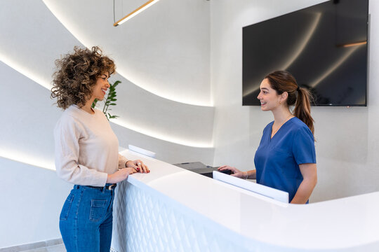 Patient at medical clinic reception. Hospital front desk, Healthcare And Medicine concept. Attractive woman talking to friendly doctor at white modern reception counter. Professional medical service.