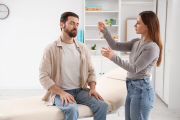 Fototapeta premium Female psychologist with pendulum hypnotizing man on couch in office