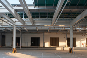 Empty large warehouse interior with concrete floor, columns, and industrial lighting.