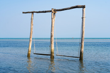 Fototapeta premium Serene Waters: A captivating beach scene features a rustic swing set emerging from the tranquil water, with the vast ocean and clear sky creating a picturesque setting.
