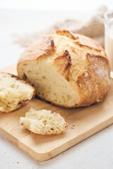 Sliced artisan sourdough bread with airy crumb on wooden board, glass of milk, and knitted cloth. Ideal for culinary, baking, and food photography projects.