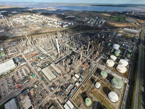 Aerial view of a sprawling industrial complex where silver tanks gleam under the sun's gaze, juxtaposed against the earth-toned landscape, Humber Refinery, Immingham, United Kingdom.