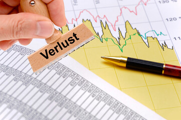 Obraz premium Ein Holzstempel ist beschriftet mit dem Aufdruck Verlust über einem Chart mit Tabellenkalkulation als Symbolbild für Gewinn oder Verlust in der Wirtschaft - FOTOMONTAGE