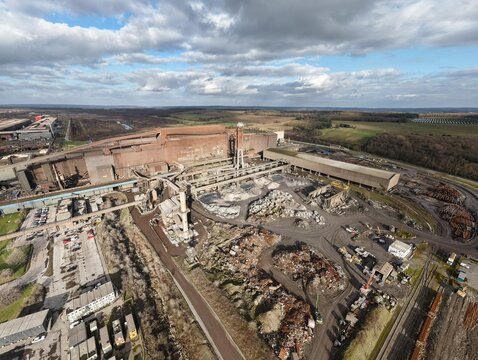 Aerial view of the vast steelworks casting long shadows under a mottled sky, industry and nature juxtaposed in stark contrast, Scunthorpe, Scunthorpe, United Kingdom.