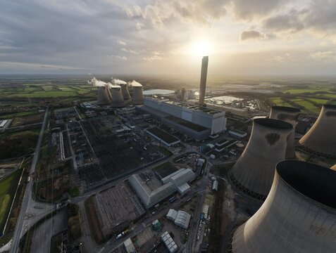 Aerial view of the immense Drax Power Station complex, its cooling towers dominating the landscape under a sky ablaze with the setting sun, Drax, Selby, United Kingdom.
