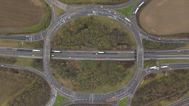 Aerial view of a busy roundabout with vehicles moving around, surrounded by lush greenery and fields, Sutton Coldfield, England, United Kingdom.