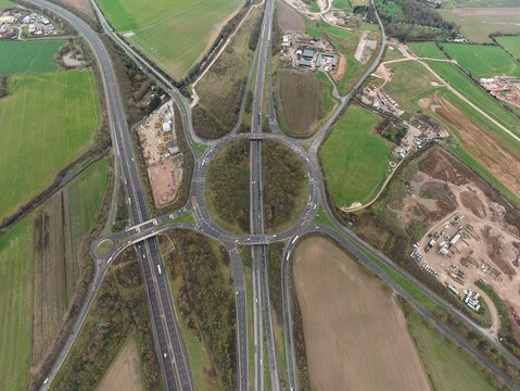 Aerial view of a complex roundabout intersection with multiple roads converging amidst a patchwork of green fields, Sutton Coldfield, England, United Kingdom.