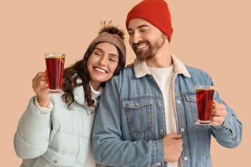Happy young couple in warm clothes with glass cups of hot mulled wine on beige background