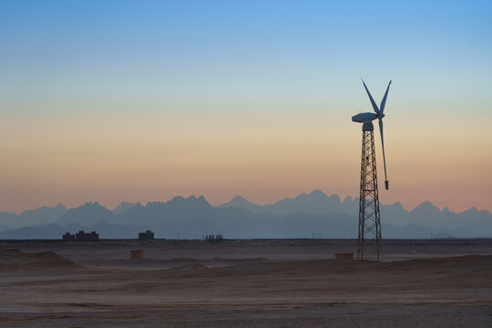 Sunset casts a warm glow over an old windmill standing gracefully in the desert, a timeless symbol of rural tranquility