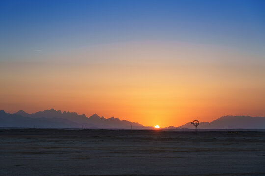 Sunset casts a warm glow over an old windmill standing gracefully in the desert, a timeless symbol of rural tranquility