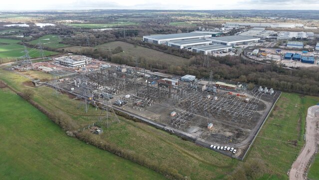 Aerial view of a sprawling electrical substation with power lines cutting through the muted greens and browns of the surrounding landscape, Birmingham, United Kingdom.