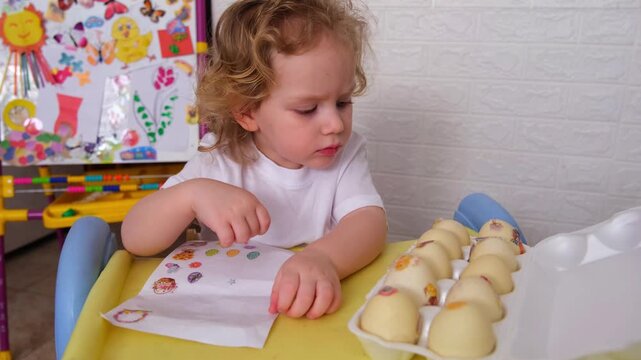 Moscow, Russia, 12.04.2025 Young child decorating Easter eggs with stickers. Happy kid adding colorful decals to egg tray for spring celebration.