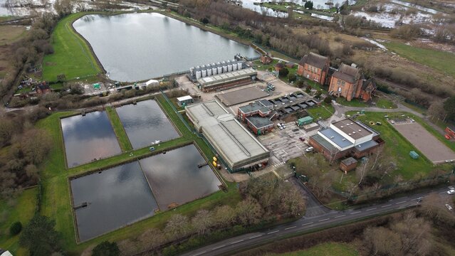 Aerial view of a complex of buildings with tanks and pools amidst a landscape of green fields and bare trees, Birmingham, England, United Kingdom.