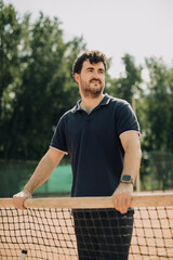 Naklejka premium Young man standing at tennis court net