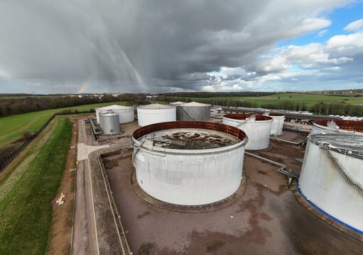 Aerial view of cylindrical tanks standing stark against the landscape under a sky pierced by a faint rainbow, Kingsbury, Tamworth, United Kingdom.