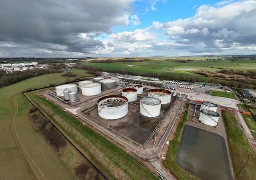 Aerial view of stark white tanks contrasting against the subdued green fields and moody skies at Kingsbury Oil Terminal, Tamworth, United Kingdom.