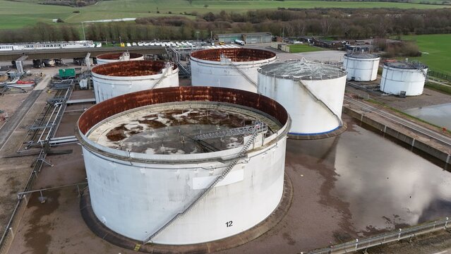 Aerial view of stark white tanks contrasted against the rusty tops and the surrounding flooded landscape at Kingsbury Oil Terminal, Kingsbury, United Kingdom.
