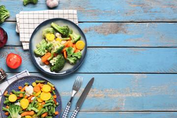 Obraz premium Plates with stewed mixed vegetables and cutlery on blue wooden background