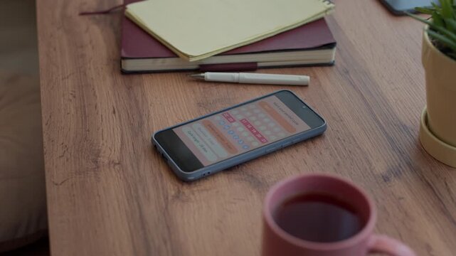 Close up handheld shot of smartphone screen with application for menstrual period tracking on home table with cup of tea and notebooks, no people
