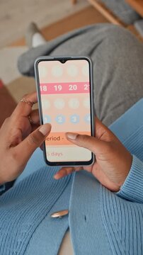 Vertical top down shot of anonymous woman checking menstrual calendar on smartphone while sitting indoors
