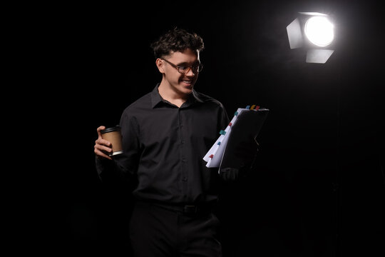 Male screenwriter with coffee reading scenario on dark background