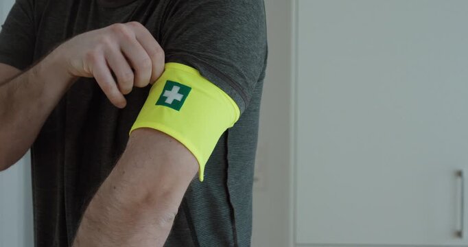 Close-up of a man adjusting a bright yellow first aid armband with a medical cross symbol, representing emergency response, preparedness, and healthcare support.