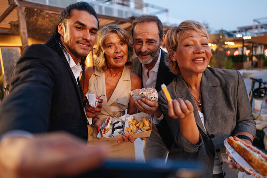 Diverse business colleagues taking a selfie while enjoying street food and laughing together after work